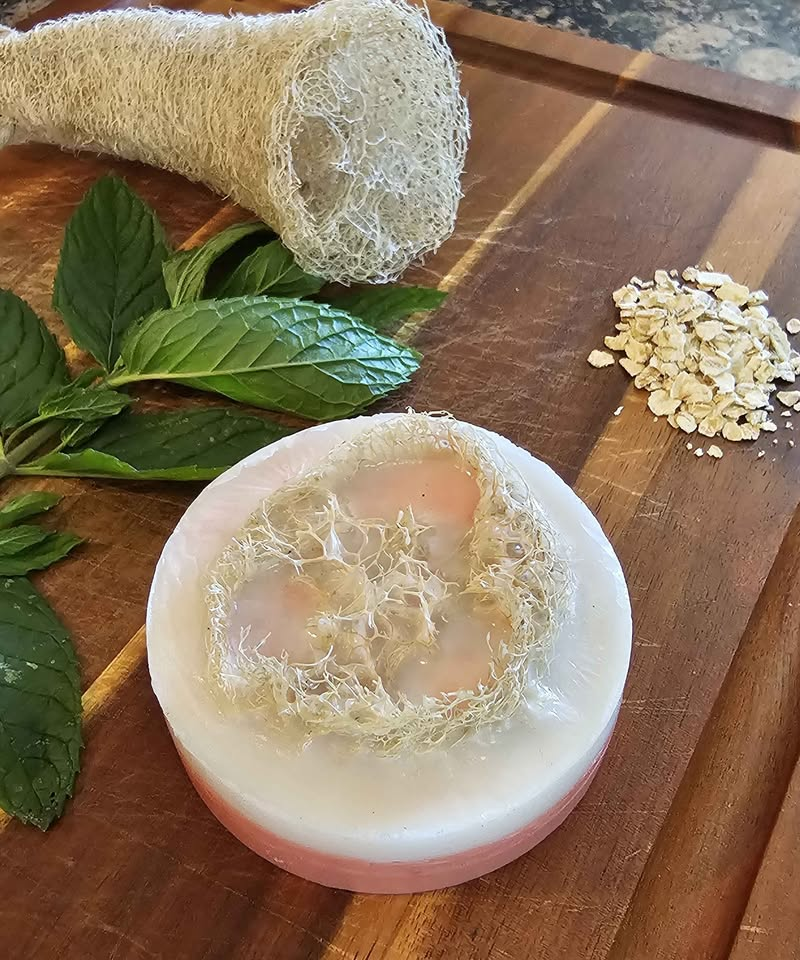 Pink peppermint loofah soap pictured with mint leaves and oats